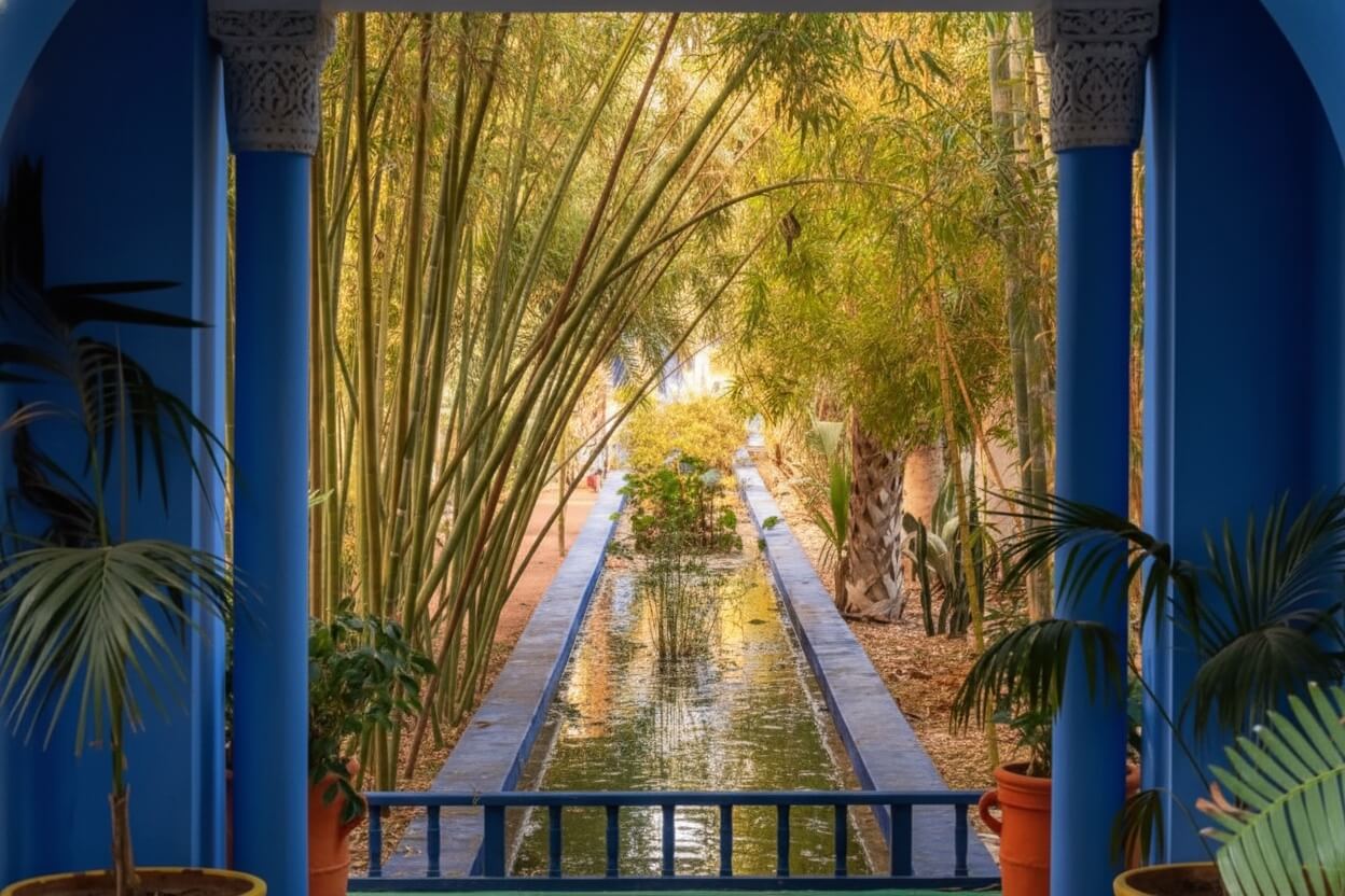 Bacino d'acqua e boschetto di bamb&ugrave; incorniciati da archi blu Majorelle